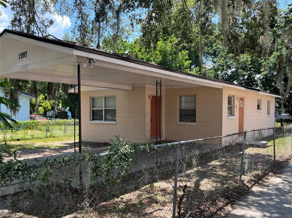 A single-story tan concrete block house features a carport and a chain-link fence — 1997 5TH STREET NE, WINTER HAVEN, FL