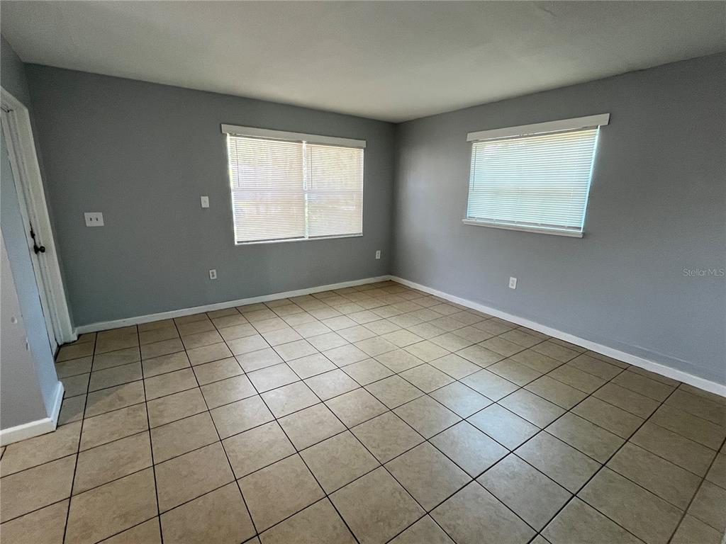 An empty room features gray walls, tan tile flooring, and two windows with white blinds — 1997 5TH STREET NE, WINTER HAVEN, FL