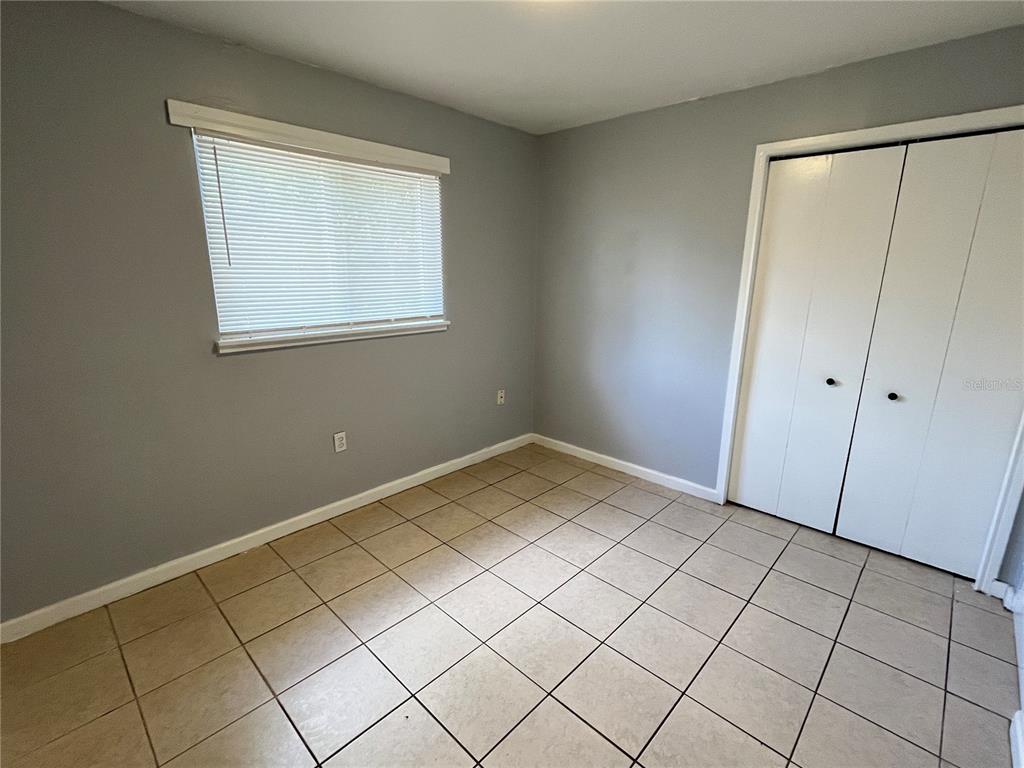 A bedroom features light gray walls, white trim, tile flooring, and a white bi-fold closet door — 1997 5TH STREET NE, WINTER HAVEN, FL