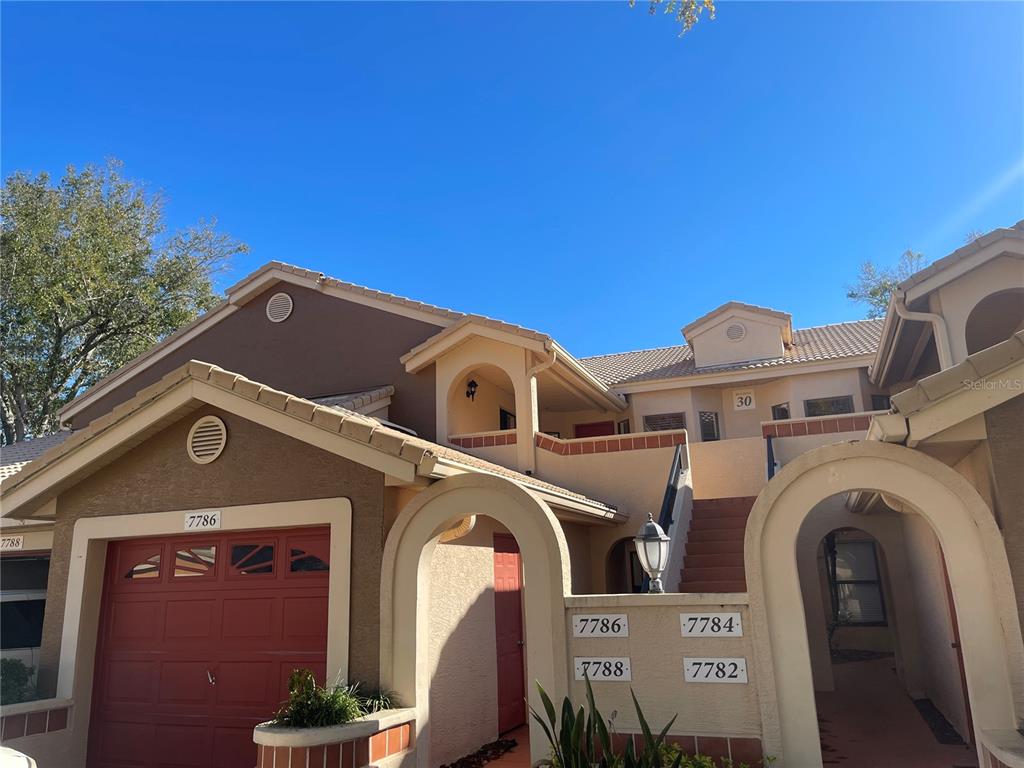 The exterior of a multi-unit residential building features stucco walls, arched entryways, and tiled roofs — 7786 SUGAR BEND DRIVE UNIT 7786, ORLANDO, FL