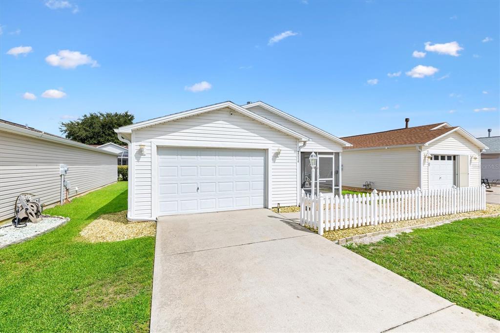 A white single-story house features a garage, a concrete driveway, and a white picket fence — 2014 JOHNSON COURT, THE VILLAGES, FL