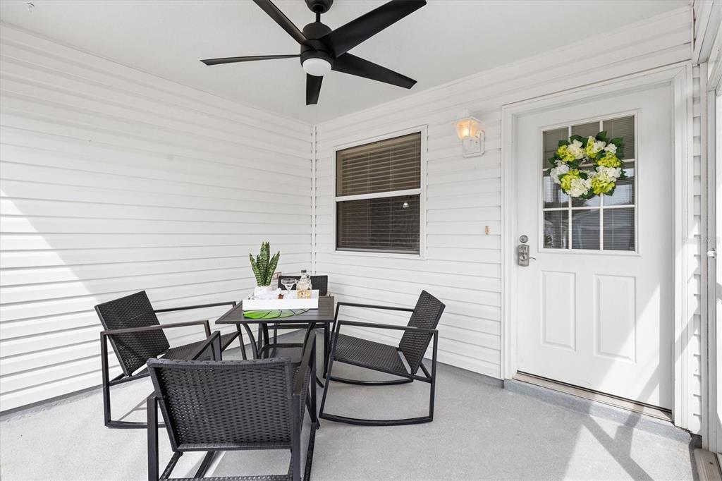 A covered patio features white siding, a ceiling fan, and a small table with chairs — 2014 JOHNSON COURT, THE VILLAGES, FL