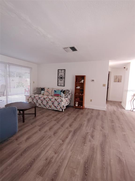 A living room features light wood-look flooring, a daybed, a wooden bookshelf, and sliding glass doors — 3425 RICHBORO DRIVE, HOLIDAY, FL
