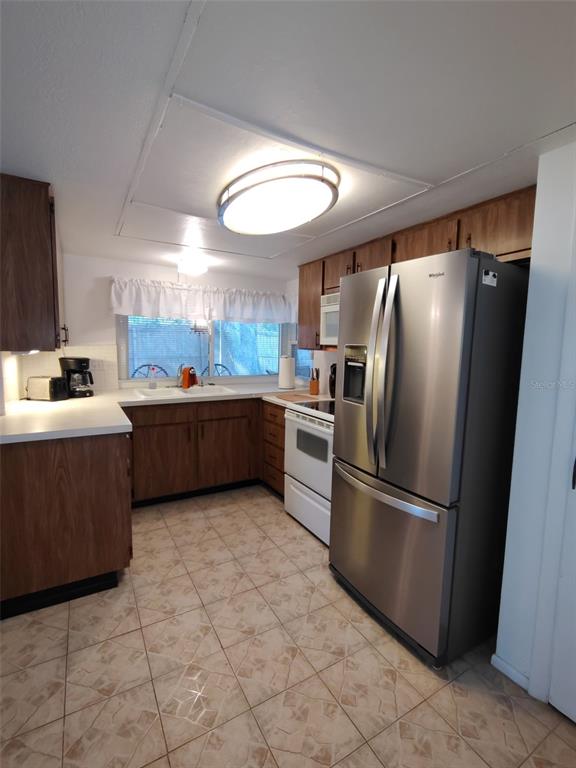 A kitchen features wood cabinets, stainless steel appliances, white countertops, and light-colored tile flooring — 3425 RICHBORO DRIVE, HOLIDAY, FL
