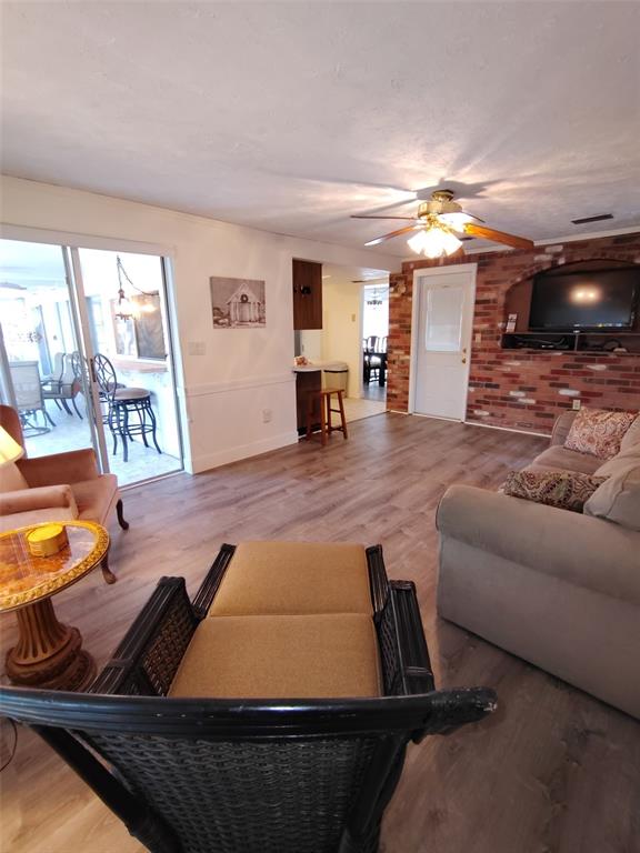 A living room features wood-look flooring, a brick accent wall with a television, and sliding doors — 3425 RICHBORO DRIVE, HOLIDAY, FL