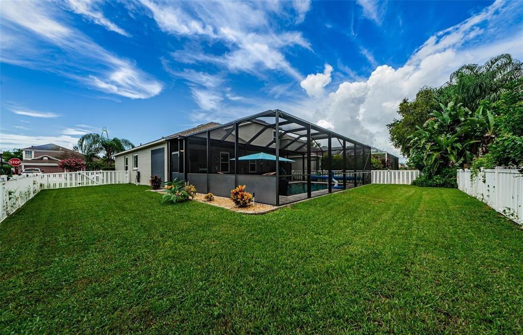A backyard with a green lawn, a white fence, and a screened-in pool enclosure — 1810 WINSLOE DRIVE, TRINITY, FL