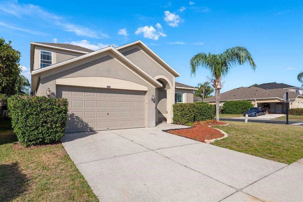 A two-story suburban house features a tan stucco exterior, a two-car garage, and a palm tree — 1810 WINSLOE DRIVE, TRINITY, FL