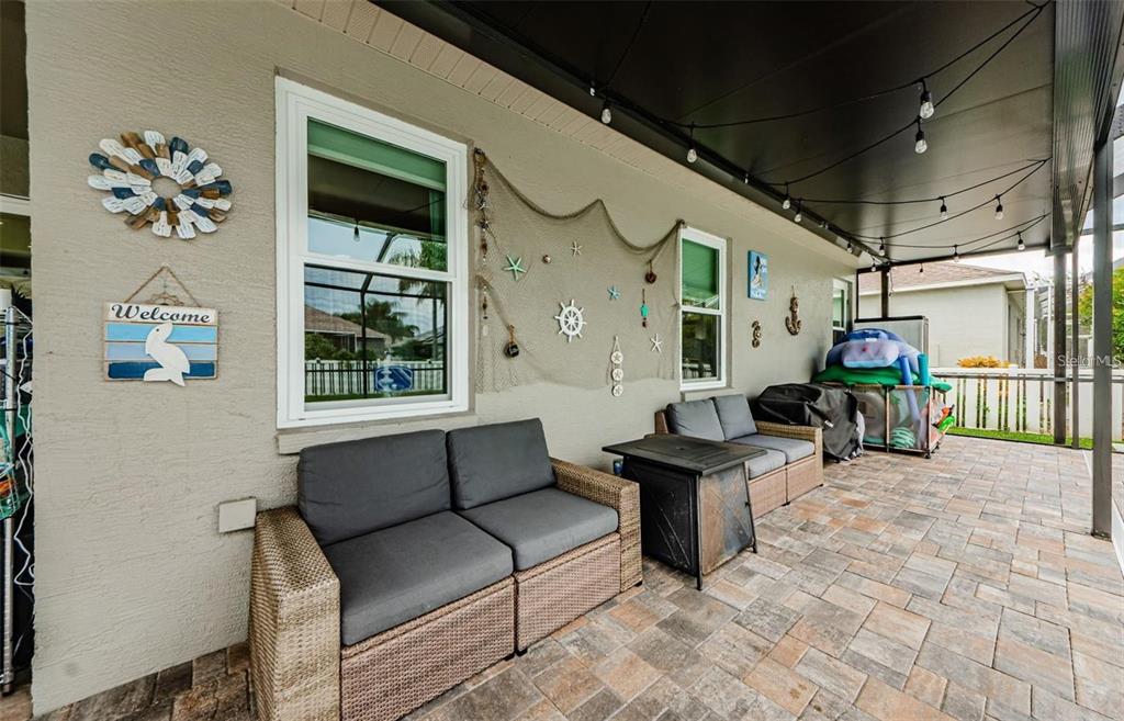 A covered patio features wicker furniture, a fire pit, and nautical wall decor on pavers — 1810 WINSLOE DRIVE, TRINITY, FL