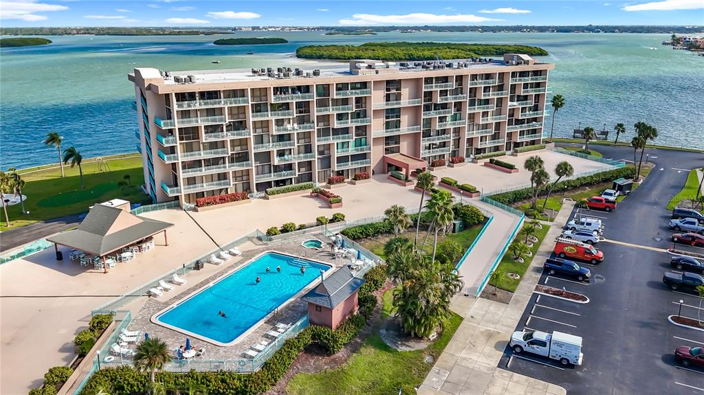 An aerial view shows a multi-story apartment building with a swimming pool and parking lot — 1 KEY CAPRI UNIT 201E, TREASURE ISLAND, FL