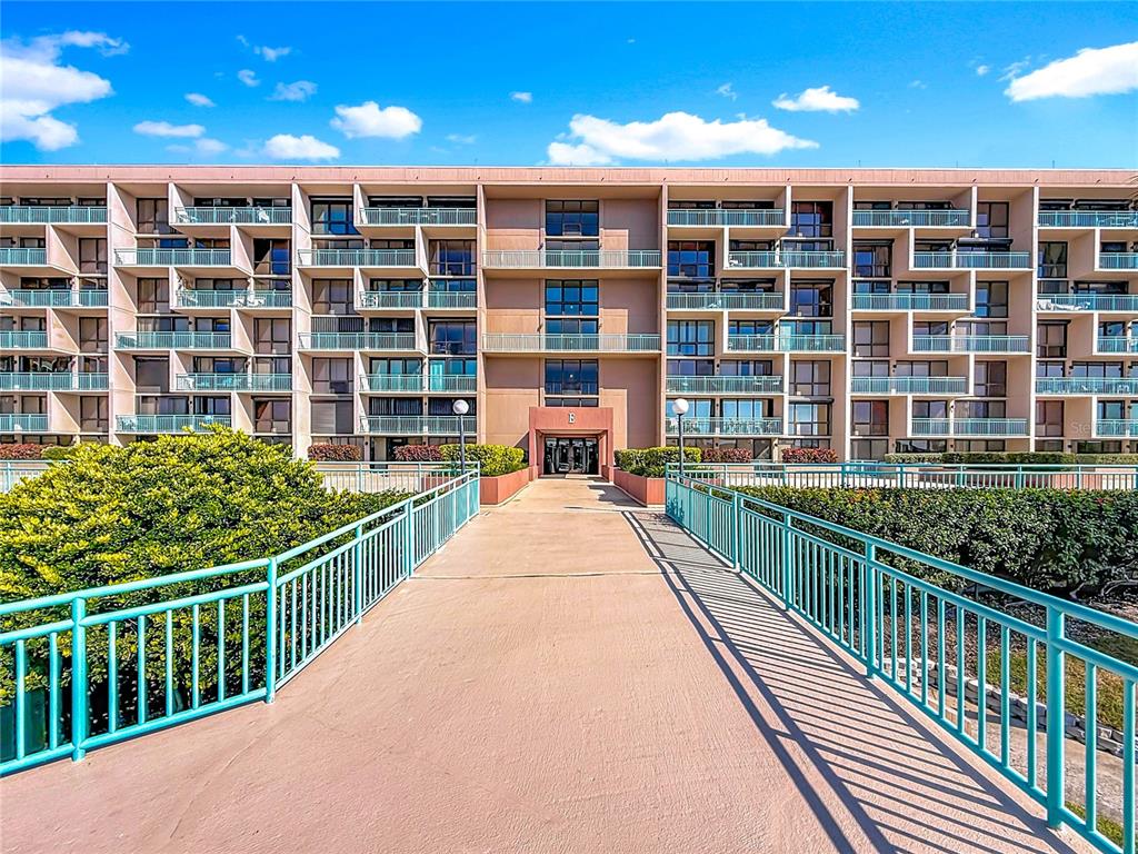 A concrete walkway with teal railings leads to the entrance of a multi-story apartment building — 1 KEY CAPRI UNIT 201E, TREASURE ISLAND, FL