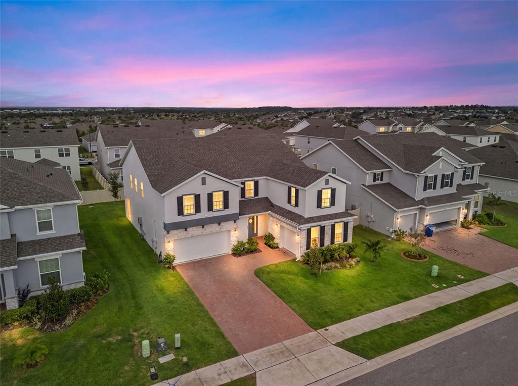An aerial view of a two-story suburban house with a brick driveway at dusk — 480 SWITCHGRASS LOOP, MINNEOLA, FL