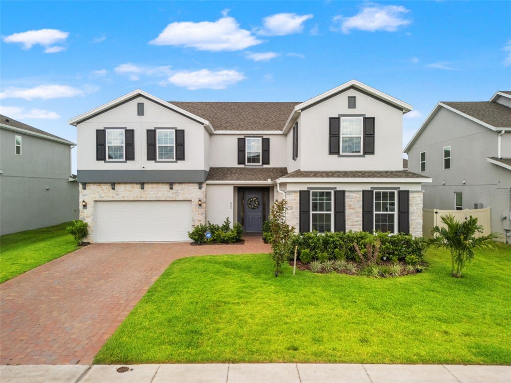 A two-story suburban house with a brick driveway, stone accents, and a two-car garage — 480 SWITCHGRASS LOOP, MINNEOLA, FL