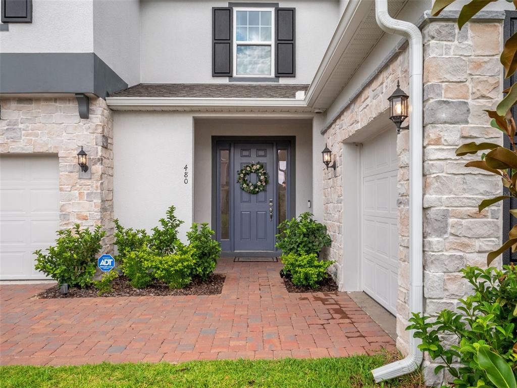 A front exterior view of a house with a gray door, stone facade, and brick walkway — 480 SWITCHGRASS LOOP, MINNEOLA, FL