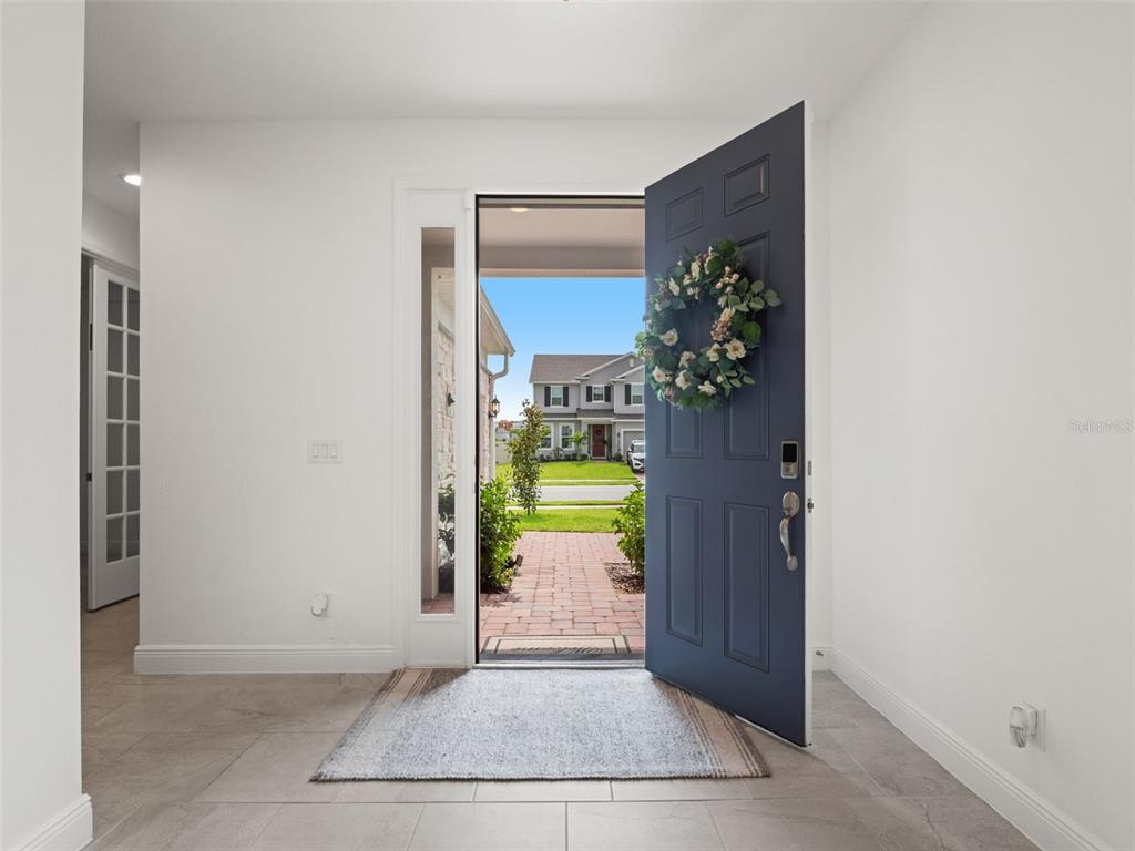 An open blue front door reveals a brick walkway and a house across the street — 480 SWITCHGRASS LOOP, MINNEOLA, FL
