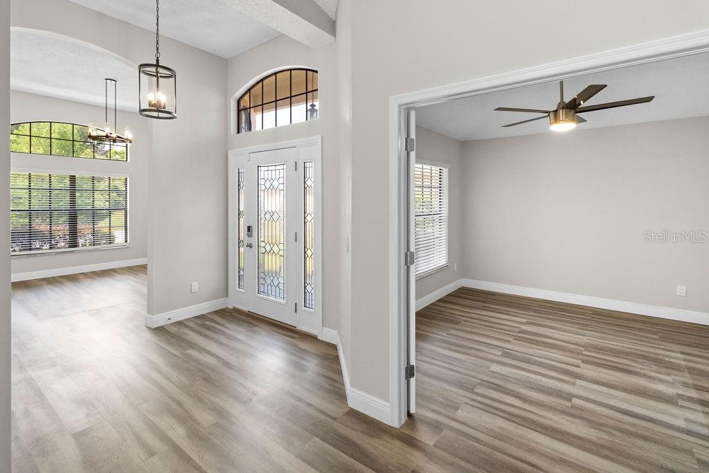 A bright room with light gray walls, wood-look flooring, a chandelier, and multiple windows — 9147 JIMINEZ DRIVE, HUDSON, FL