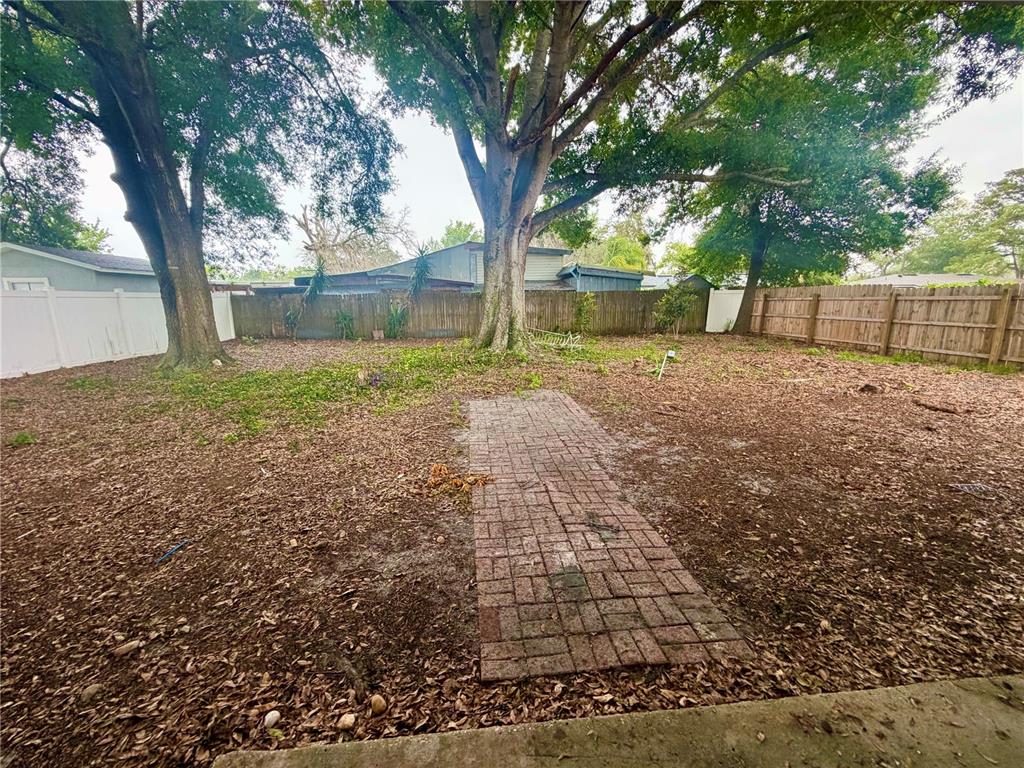 A backyard features a brick path leading toward large trees and a wooden fence — 464 NEW MEADOWS COURT, OCOEE, FL