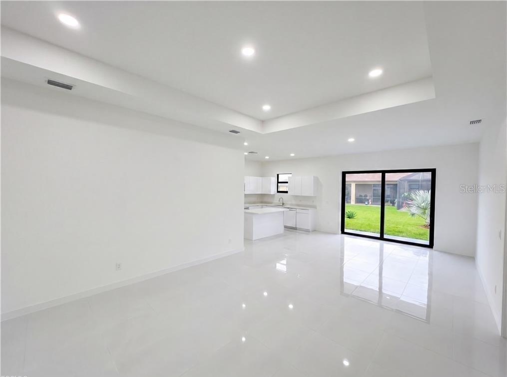 A bright, open-concept living area with white tile floors, a tray ceiling, and a kitchen — 4333 NW 34TH LANE, CAPE CORAL, FL