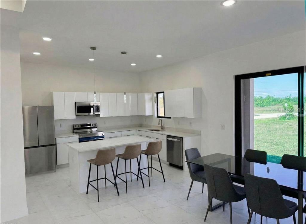 A modern kitchen features white cabinets, stainless steel appliances, a center island, and dining area — 4333 NW 34TH LANE, CAPE CORAL, FL