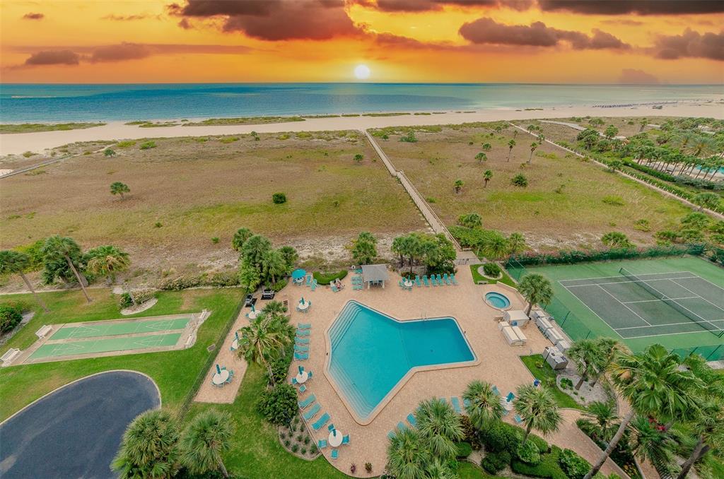 An aerial view shows a multi-story apartment building with a tennis court and swimming pool — 1250 GULF BOULEVARD UNIT 703, CLEARWATER BEACH, FL