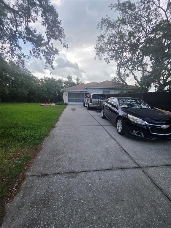 A concrete driveway leads to a house with a garage and two parked vehicles — 17820 MONTEVERDE DRIVE, SPRING HILL, FL