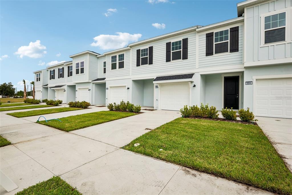 A row of light blue townhouses with white garage doors and small front lawns — 6848 HOLCOMBE DOWN DRIVE, ZEPHYRHILLS, FL