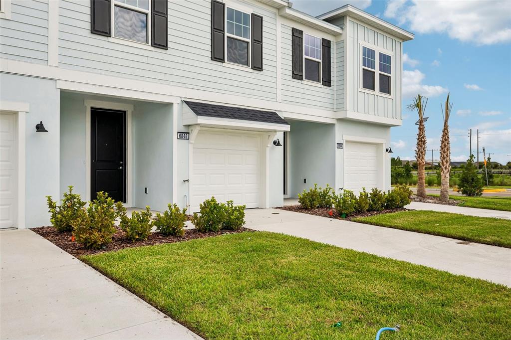 A light blue two-story townhouse exterior features a white garage and a black front door — 6848 HOLCOMBE DOWN DRIVE, ZEPHYRHILLS, FL