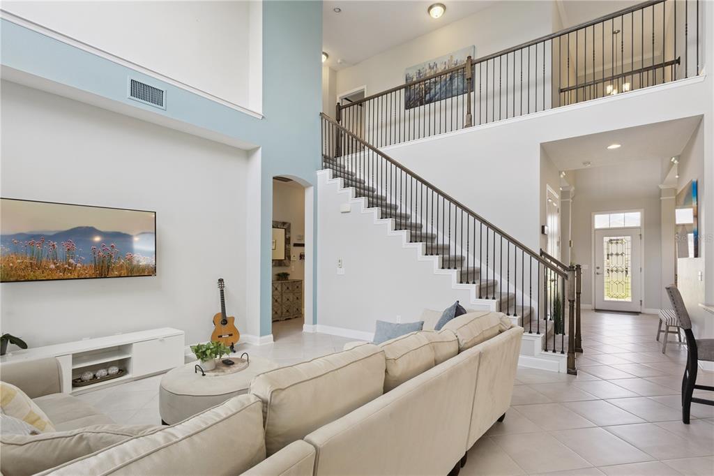 A living room with a large sectional sofa, a round ottoman, and an open staircase — 16416 GOOD HEARTH BOULEVARD, CLERMONT, FL