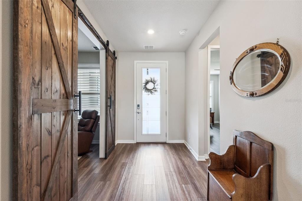 A bright entryway features wood-look flooring, a white front door, and rustic sliding barn doors — 2701 TIMBERGROVE STREET, ST CLOUD, FL
