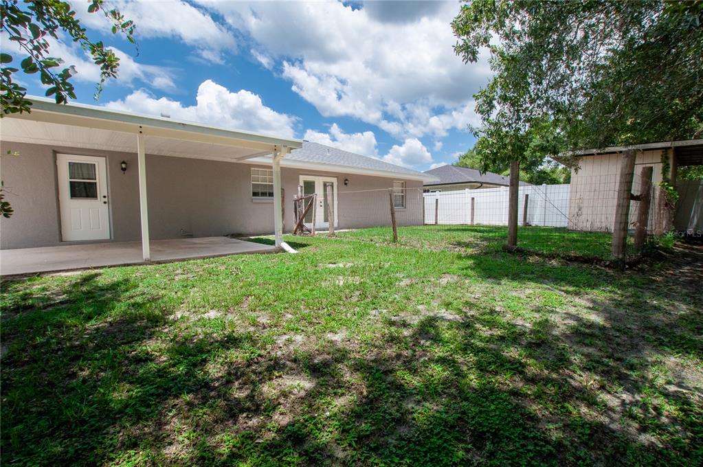 A backyard view of a house with a covered patio, lawn, and a small shed — 1204 E GIBSON STREET, ARCADIA, FL