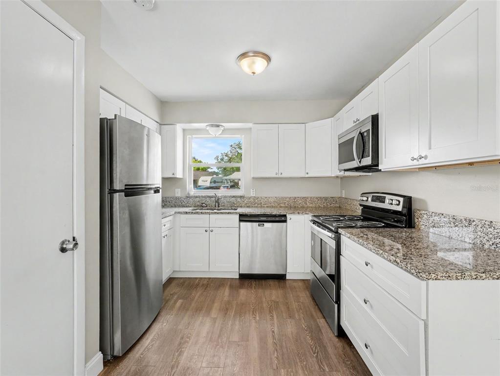 A kitchen features white cabinets, granite countertops, stainless steel appliances, and wood-look flooring — 308 VANIMAN AVENUE, WINTER HAVEN, FL