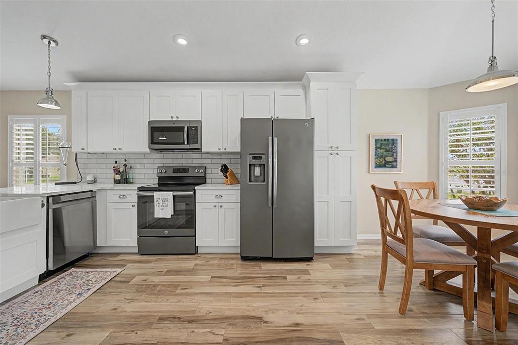 A kitchen features white cabinetry, stainless steel appliances, a subway tile backsplash, and wood flooring — 1004 SWEET JASMINE DRIVE, TRINITY, FL