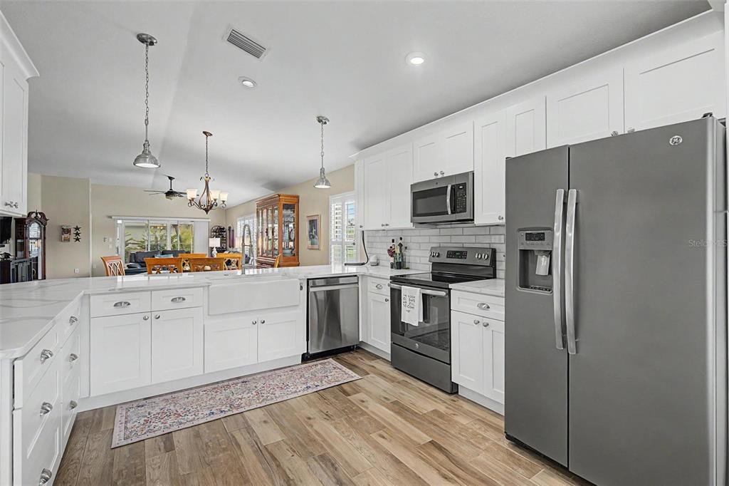 A kitchen with white cabinets, stainless steel appliances, a farmhouse sink, and wood-look flooring — 1004 SWEET JASMINE DRIVE, TRINITY, FL
