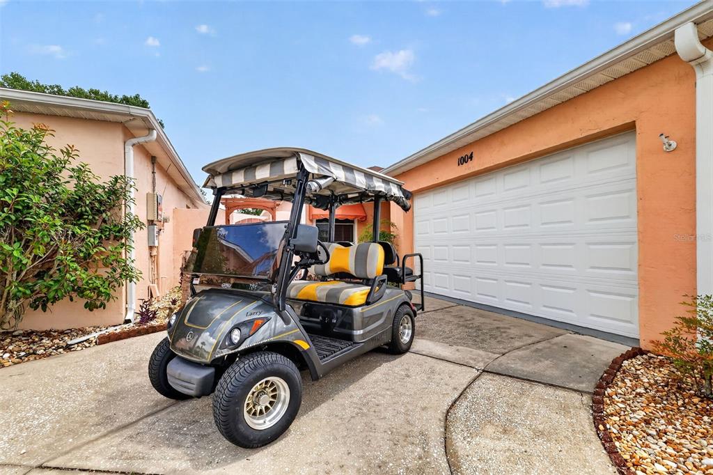 A golf cart with a striped canopy is parked on a concrete driveway before a garage — 1004 LAREDO LANE, LADY LAKE, FL