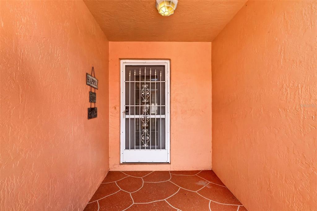 A covered entryway features peach-colored walls, a white security screen door, and tiled flooring — 1004 LAREDO LANE, LADY LAKE, FL