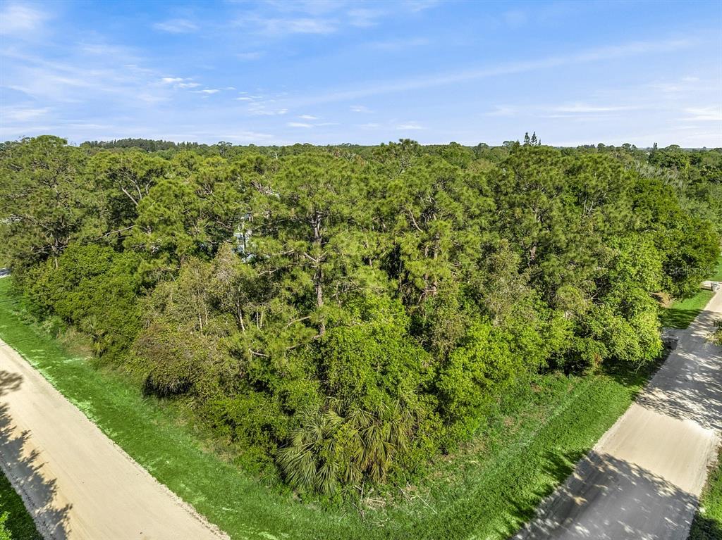 An aerial view shows a wooded, undeveloped corner lot bordered by two dirt roads — 2115 86TH DRIVE, VERO BEACH, FL