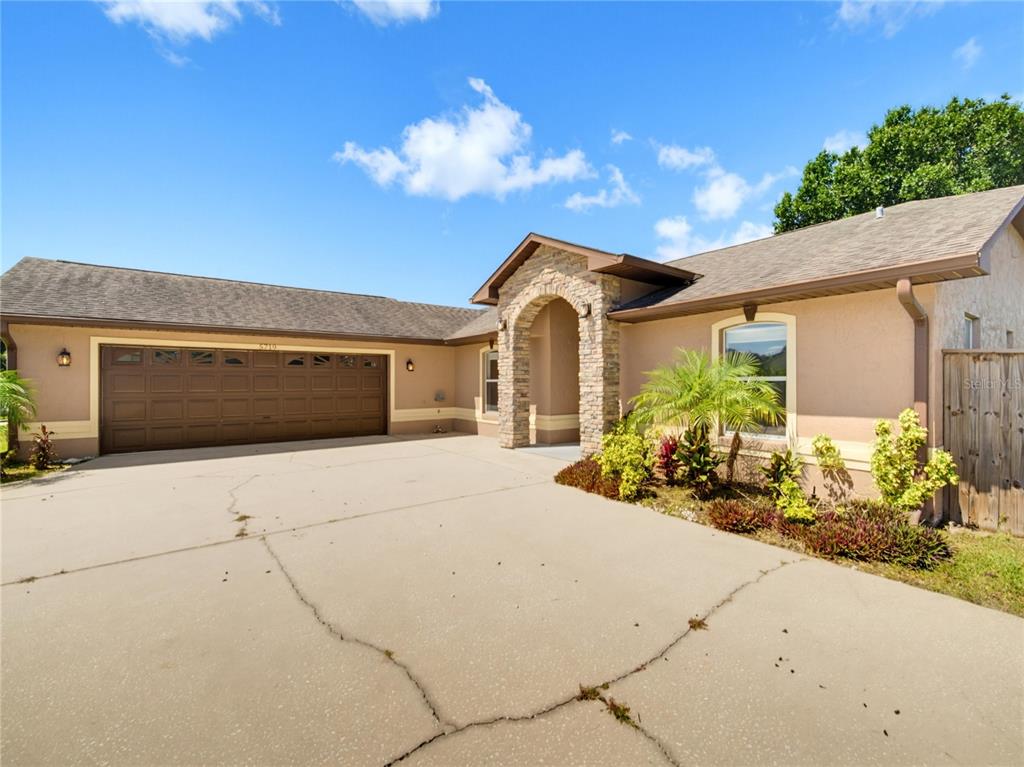 The exterior of a single-story house features a stone-accented entryway and a concrete driveway — 5719 SWEETHEART COURT, ST CLOUD, FL