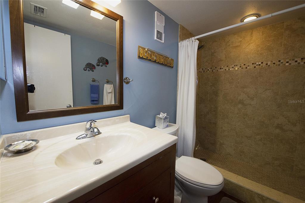 A bathroom features a wood vanity, blue walls, a mirror, and a tiled shower area — 1571 S ATLANTIC AVENUE UNIT 307, NEW SMYRNA BEACH, FL