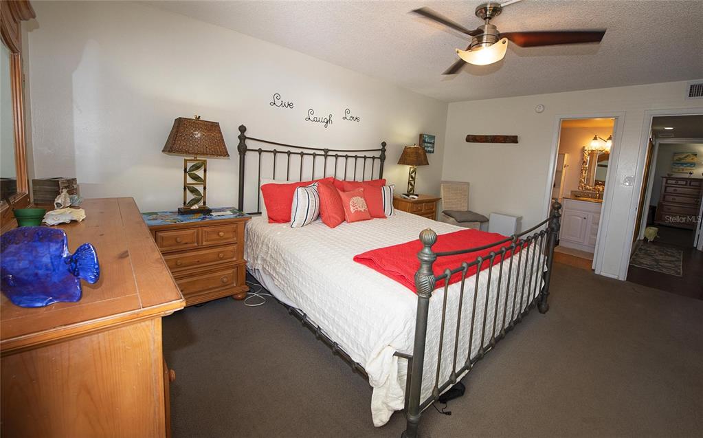 A bedroom features a metal-framed bed, wooden furniture, and a ceiling fan over carpeted floors — 1571 S ATLANTIC AVENUE UNIT 307, NEW SMYRNA BEACH, FL