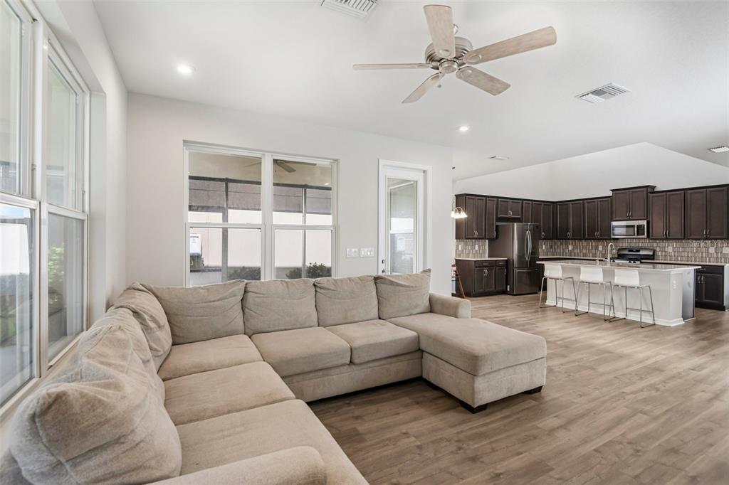 A living room with a large sectional sofa opens into a kitchen with dark cabinetry — 13690 STEVENSON LANE, ODESSA, FL