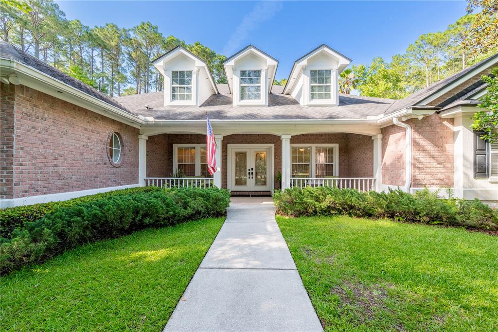 A brick house exterior features a covered porch, a central walkway, and three roof dormers — 104 BELMONT DRIVE, ST JOHNS, FL