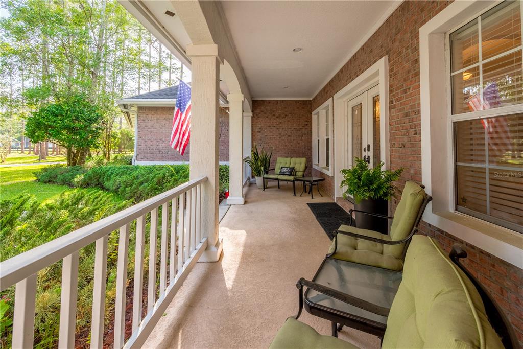 A covered brick porch features a white railing, green patio furniture, and an American flag — 104 BELMONT DRIVE, ST JOHNS, FL