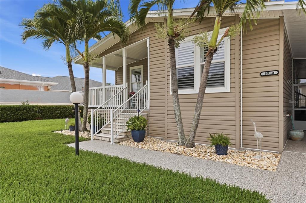 A tan mobile home with a front porch, palm trees, and a landscaped yard — 3530 70TH AVENUE E, ELLENTON, FL