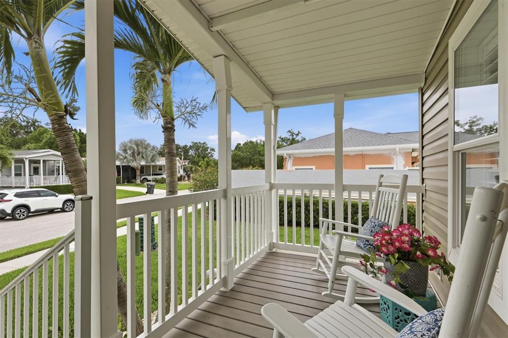 A covered porch features white railings, wooden decking, and two rocking chairs with floral cushions — 3530 70TH AVENUE E, ELLENTON, FL