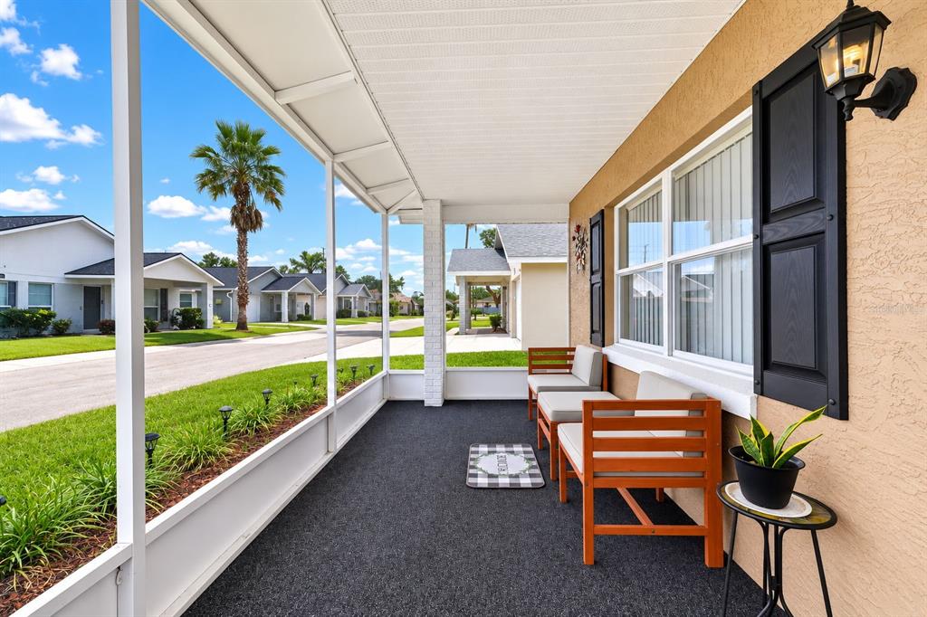 A screened-in porch features dark carpeting, wooden chairs, and a view of a residential street — 4772 SILVER CIRCLE, ZEPHYRHILLS, FL