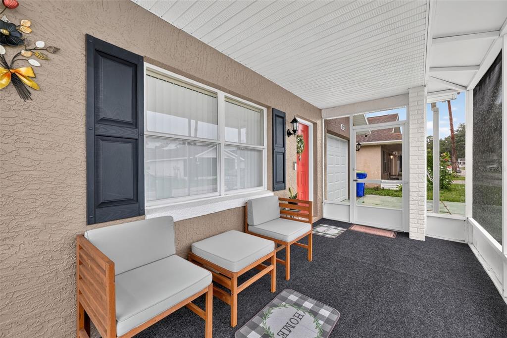 A covered porch features gray outdoor chairs, a small table, and a red front door — 4772 SILVER CIRCLE, ZEPHYRHILLS, FL