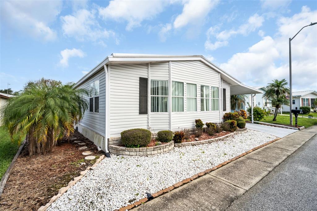 A single-story manufactured home with white siding, a gravel yard, and a palm tree — 428 PELICAN DRIVE S, OLDSMAR, FL