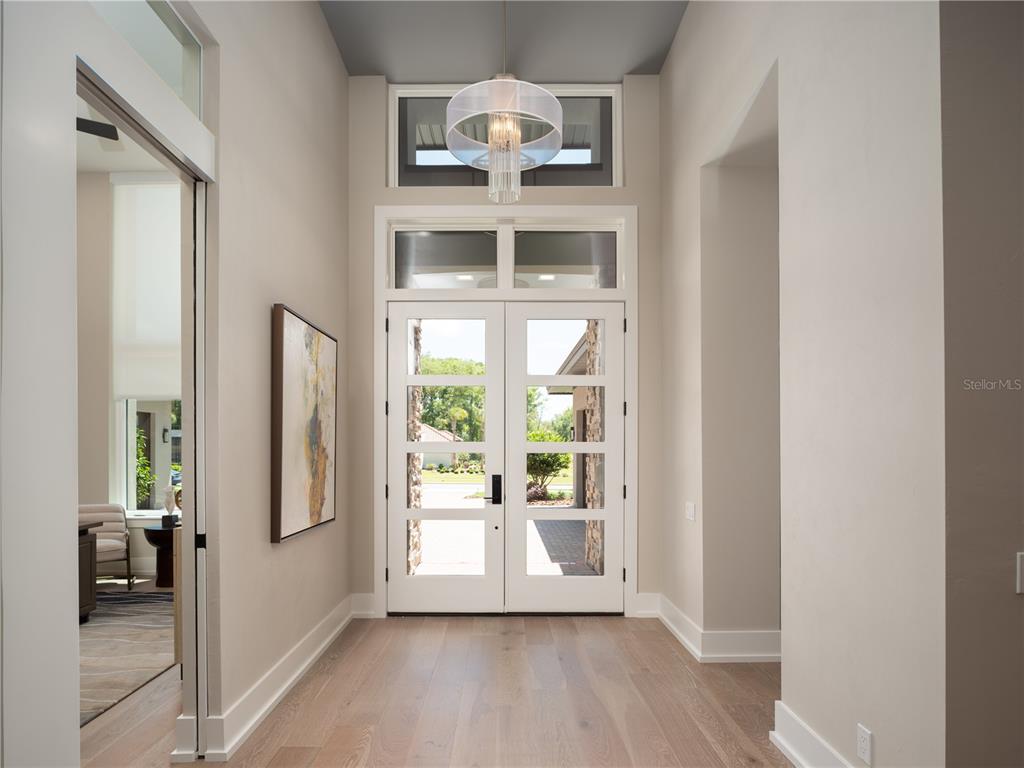 A bright entryway features light wood floors, a modern chandelier, and white double glass doors — 3120 SW 108TH WAY, GAINESVILLE, FL