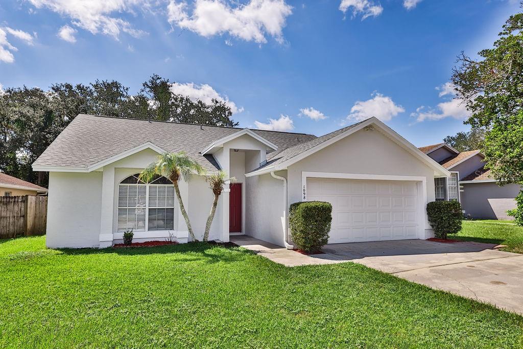 A single-story house with a white exterior, a two-car garage, and a red front door — 1098 SUGARBERRY TRAIL, OVIEDO, FL