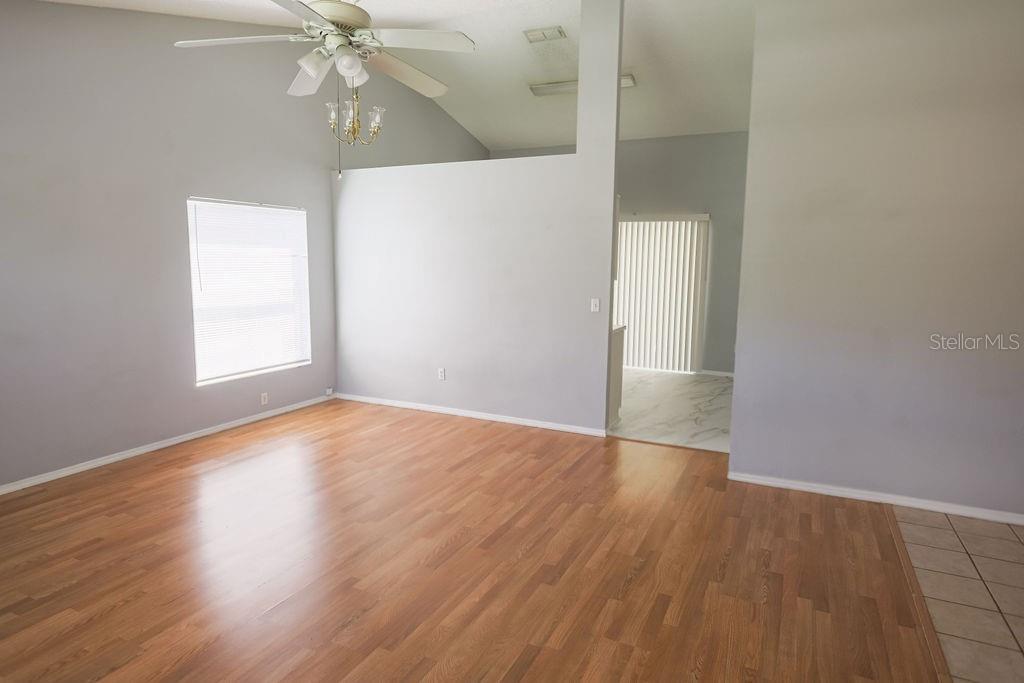 An empty living room features light gray walls, wood-look flooring, and a vaulted ceiling — 1098 SUGARBERRY TRAIL, OVIEDO, FL