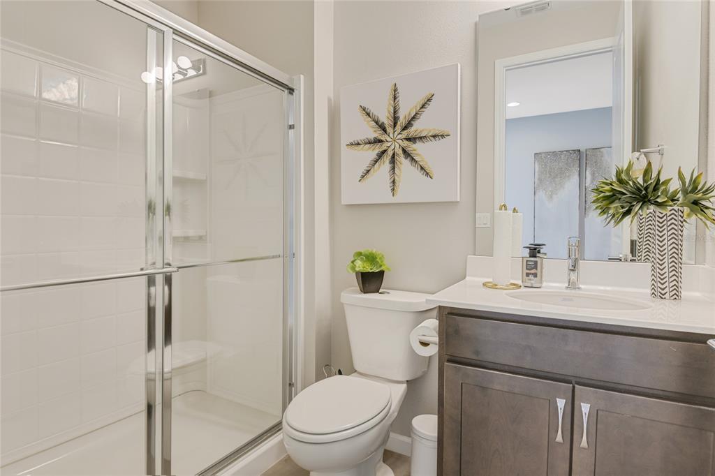 A bathroom features a glass-enclosed shower, a white toilet, and a dark wood vanity — 10113 TURNBERRY LANE, LEESBURG, FL